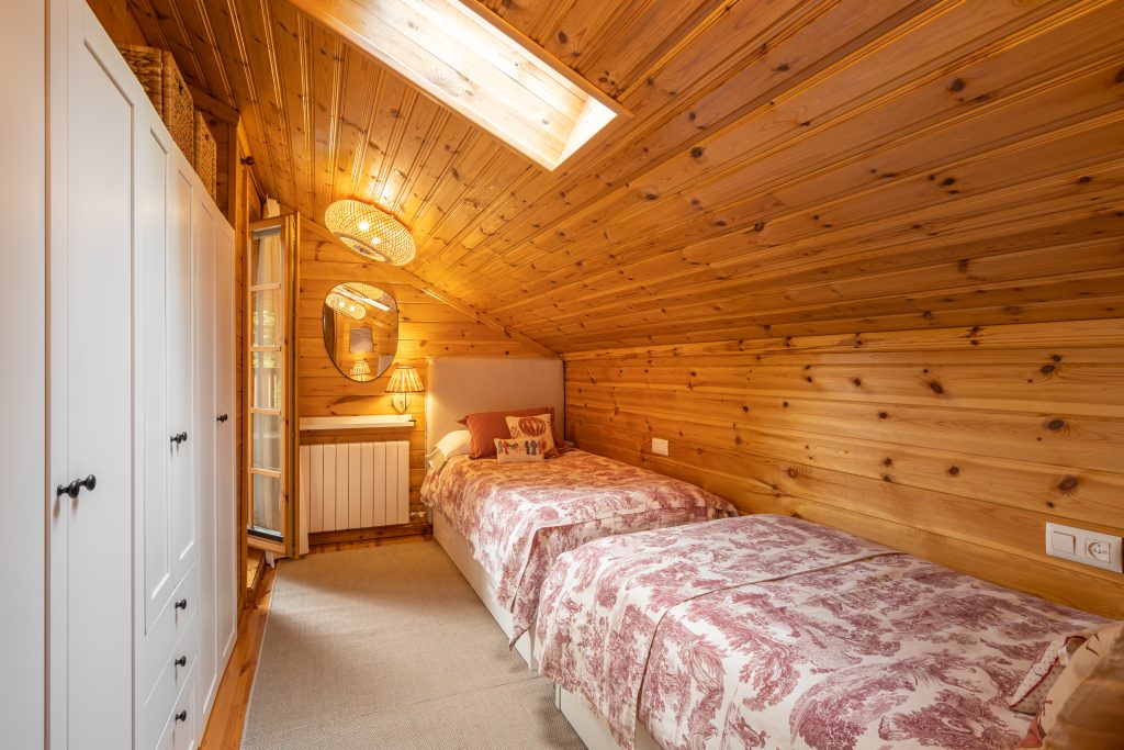 Cozy bedroom with two beds and white wardrobe in a modern cottage with wooden walls.